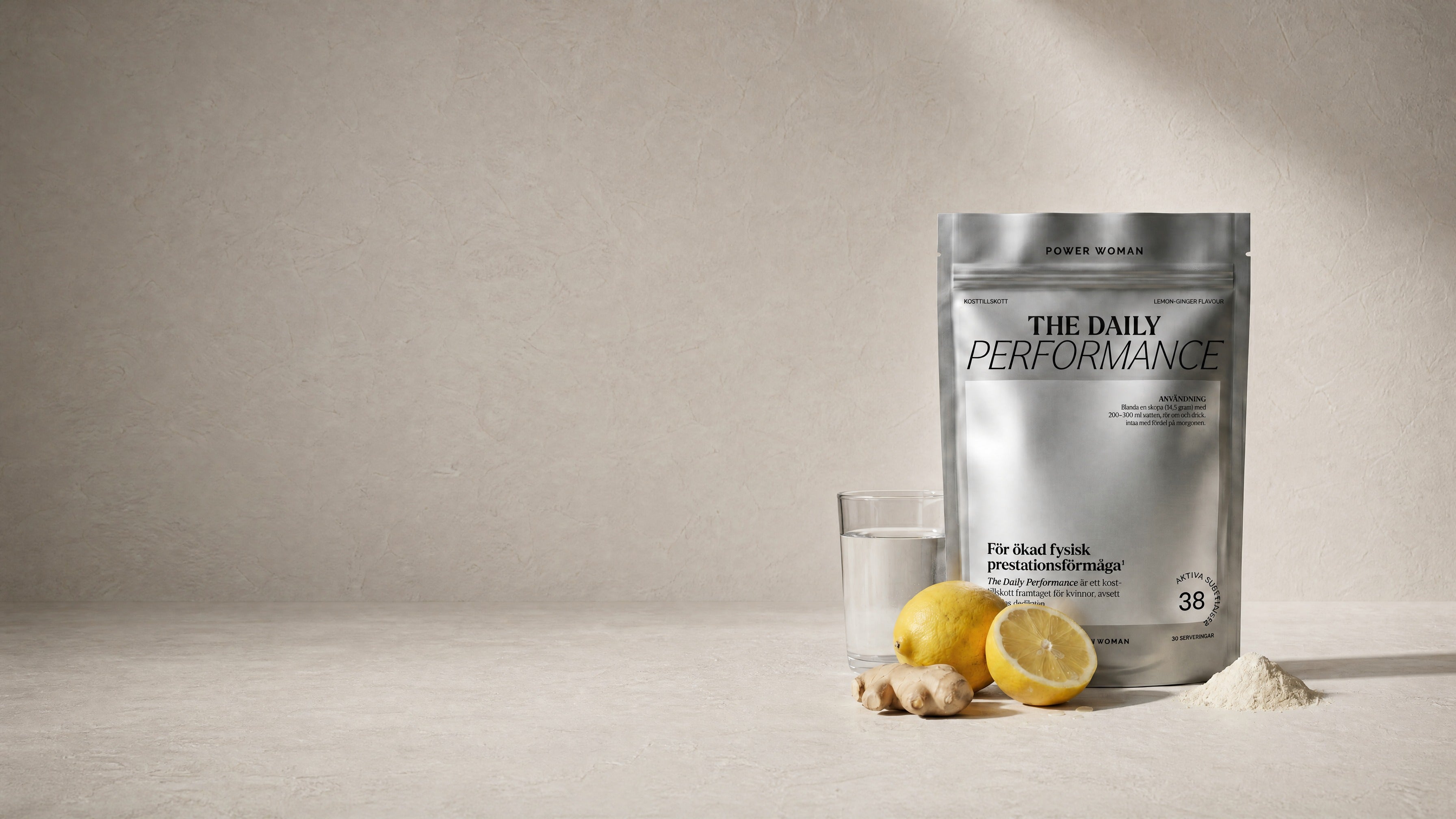 A silver stand-up pouch of 'The Daily Performance' protein powder by Power Women stands on a light beige surface next to a glass of water, fresh lemons, ginger root, and a small pile of powder.