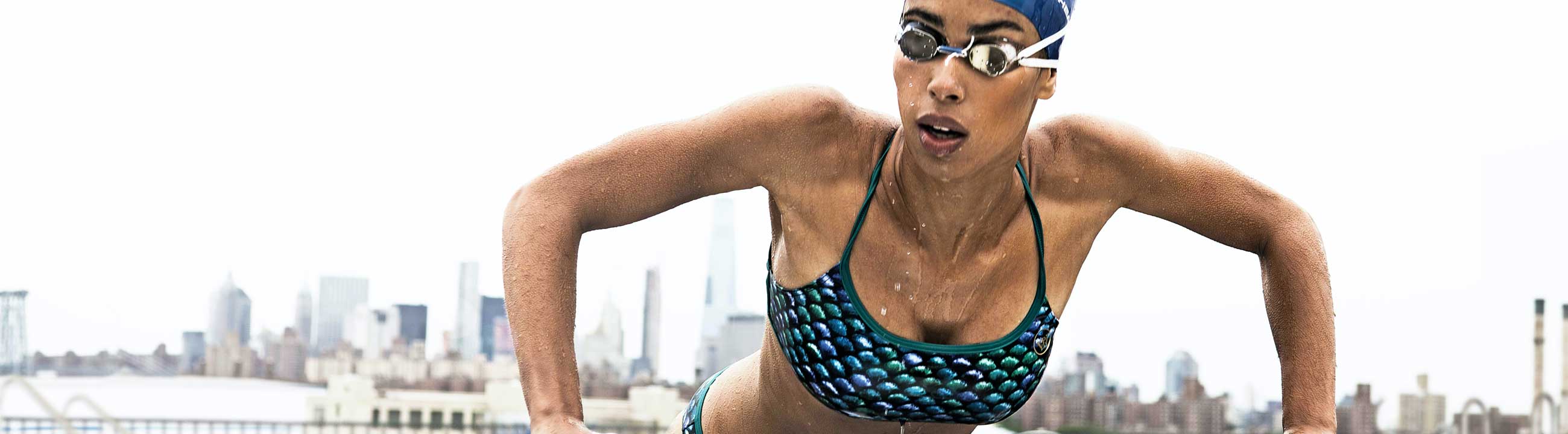 Athlete getting out of a pool in a multicolor bikini with a city skyline background